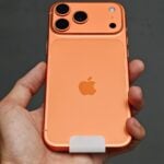 Hand holding an orange smartphone with three cameras